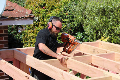 Carpenter wearing Mufftech Orange Roughy hearing protection while framing a roof on site