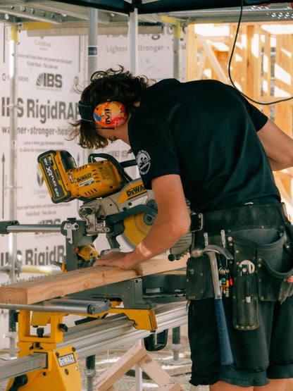Builder cutting timber on a mitre saw while wearing Mufftech Orange Roughy noise-reducing earmuffs