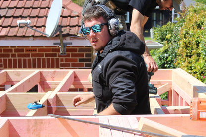 Builder framing a roof outdoors while wearing Mufftech Sole Bluetooth earmuffs